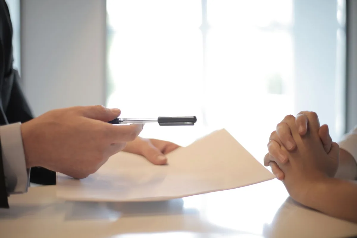 Hands exchanging a pen and policy document to sign auto insurance coverage